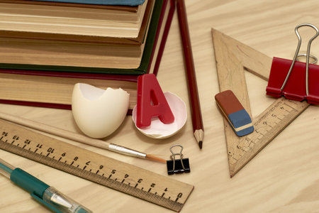 a stack of books writing materials stationery clips and a split chicken egg with the letter A inside...