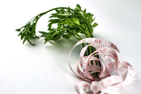 green parsley leaves measuring tape and fork on a white background concept diet vegetarianism veganism. high quality photoの写真素材