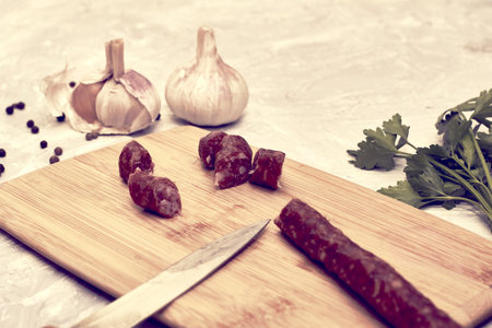 spicy smoked sausages on a cutting board next to red pepper garlic spices and herbs on the table....
