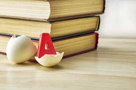 a stack of books and a split chicken egg with the letter a inside on the table the concept of knowledge education school. high quality photoの写真素材