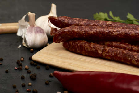 spicy smoked sausages on a cutting board next to red pepper garlic and herbs on a black background. high quality photoの写真素材