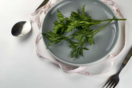 a plate of greens wrapped with a measuring tape next to a fork and spoon the concept of vegetarianism veganism diet. high quality photoの写真素材