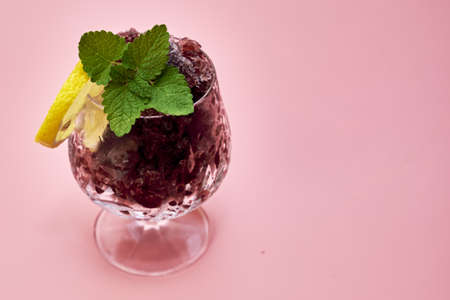 frozen red wine in a glass glass decorated with a slice of lemon and lemon leaves on a pink background copy space . high quality photoの写真素材