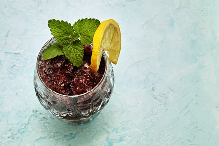frozen red wine in a glass glass decorated with a slice of lemon and lemon leaves on a blue...