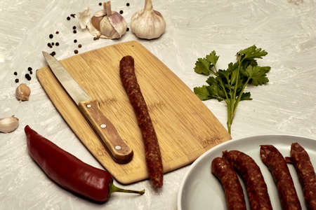 spicy smoked sausages on a cutting board next to red pepper garlic spices and herbs on the table. high quality photoの写真素材