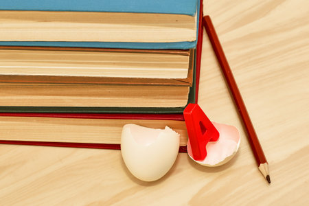 a stack of books a pencil and a split chicken egg with the letter a inside on the table the concept...