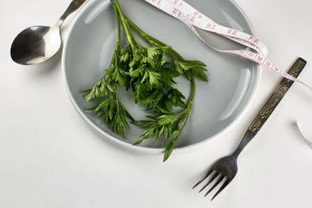 a plate of greens wrapped with a measuring tape next to a fork and spoon the concept of vegetarianism veganism diet. high quality photoの写真素材