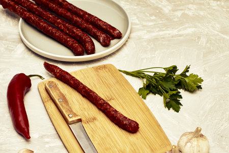 spicy smoked sausages on a cutting board next to red pepper garlic spices and herbs on the table....