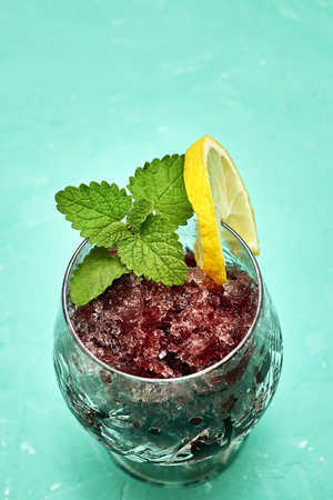frozen red wine in a glass glass decorated with a slice of lemon and lemon leaves on a green...