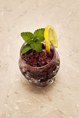 frozen red wine in a glass glass decorated with a slice of lemon and lemon leaves on a beige background. high quality photoの写真素材