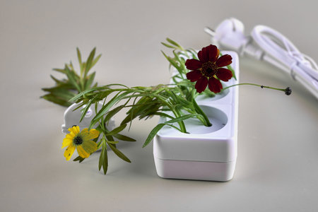electric extension cord with plug inserted into it from which grass and flowers grow concept ecology...