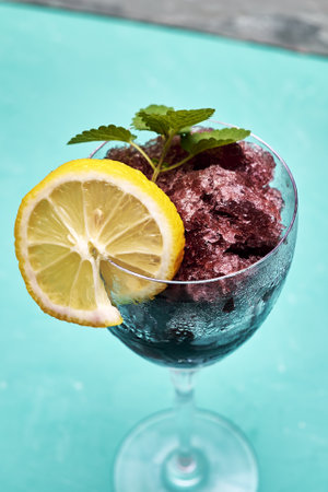 frozen red wine in a glass glass decorated with a slice of lemon and lemon leaves on a blue background copy space. high quality photoの写真素材