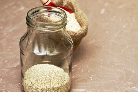 quinoa cereal with a wooden spoon is stuffed into a canvas bag and a glass jar on the table. high quality photoの写真素材