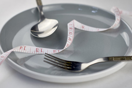 fork spoon and measuring tape on a gray plate diet conceptの写真素材