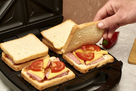 a man cooking sandwiches in a sandwich maker puts a piece of bread in a mold. high quality photoの写真素材