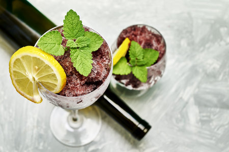 frozen red wine in two glass glasses decorated with a slice of lemon and lemon leaves and an empty glass bottle. high quality photoの写真素材