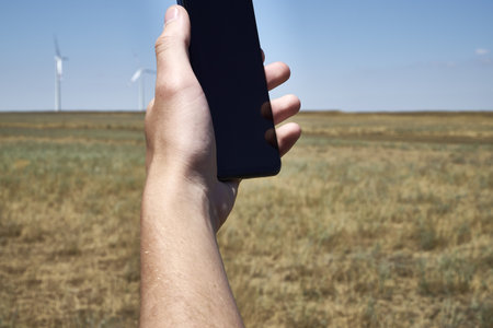 a man holds a smartphone in his hand against the background of a modern wind farm. mobile phone communication. Modern communication. high quality photoの写真素材
