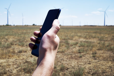 a man holds a smartphone in his hand against the background of a modern wind farm. mobile phone communication. Modern communication. high quality photoの写真素材