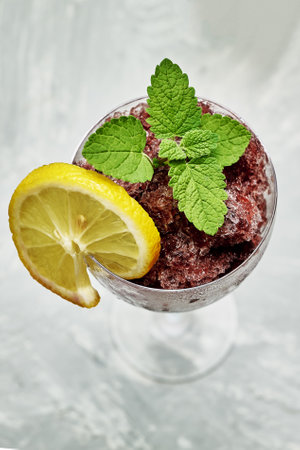 frozen red wine in a glass glass decorated with a slice of lemon and lemon leaves on a gray background. high quality photoの写真素材