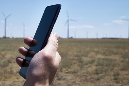 a man holds a smartphone in his hand against the background of a modern wind farm. mobile phone...