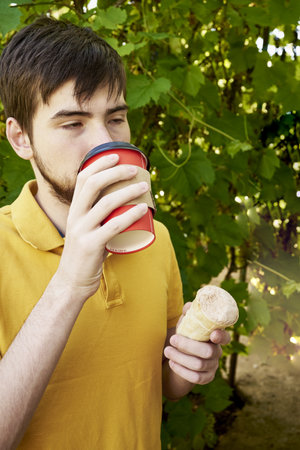 a young guy of 20 years old drinks coffee and eats ice cream in the garden on a summer day. high quality photoの写真素材
