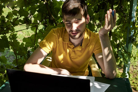 a young businessman is working at a computer in the garden on a sunny summer day the concept of remote work at home. high quality photoの写真素材
