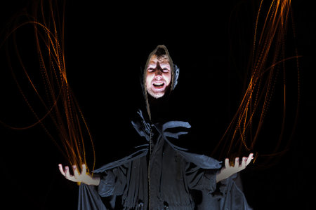 a sorcerer in a black cloak throws fire from his hands on a black background Halloween concept. high quality photoの写真素材