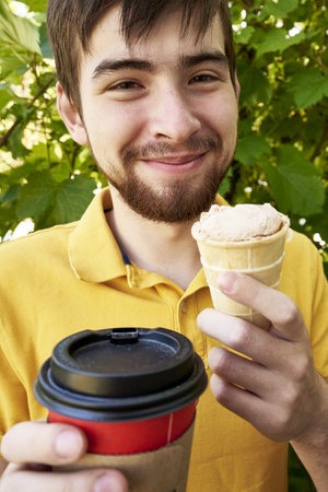 a young guy of 20 years old eats ice cream and drinks coffee in the garden on a summer day. high quality photoの写真素材