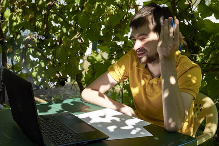 a young businessman is working at a computer in the garden on a sunny summer day the concept of remote work at home. high quality photoの写真素材