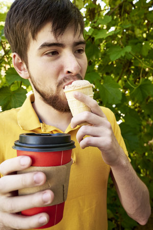 a young guy of 20 years old eats ice cream and drinks coffee in the garden on a summer day. high quality photoの写真素材