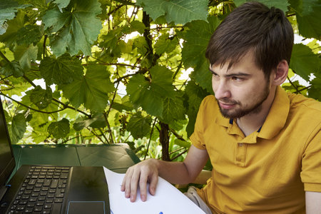 a young businessman is working at a computer in the garden on a sunny summer day the concept of remote work at home. high quality photoの写真素材
