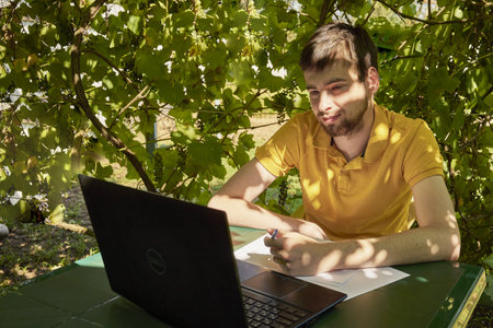 a young businessman is working at a computer in the garden on a sunny summer day the concept of remote work at home. high quality photoの写真素材