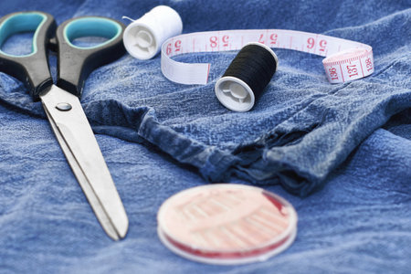 scissors needles measuring tape and thread on the background of torn jeans the concept of reasonable consumption of needlework for small businesses. high quality photoの写真素材
