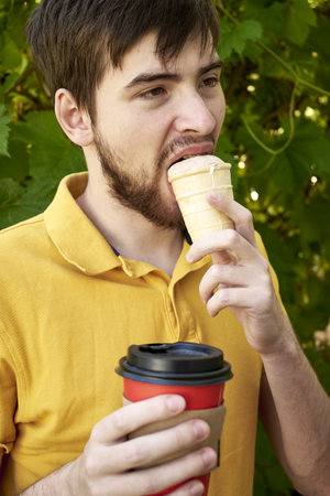 a young guy of 20 years old eats ice cream and drinks coffee in the garden on a summer day. high quality photoの写真素材