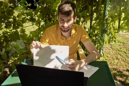 a young businessman is working at a computer in the garden on a sunny summer day the concept of remote work at home. high quality photoの写真素材