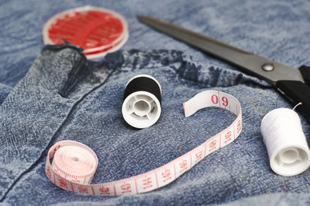 scissors needles measuring tape and thread on the background of torn jeans the concept of reasonable consumption of needlework for small businesses. high quality photoの写真素材