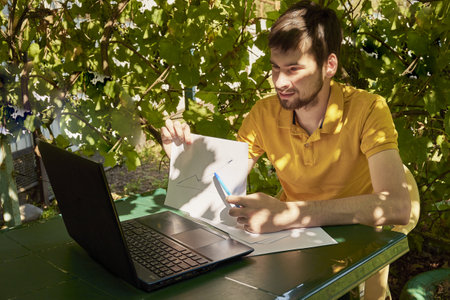 a young businessman is working at a computer in the garden on a sunny summer day the concept of remote work at home. high quality photoの写真素材