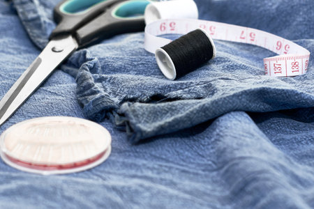 scissors needles measuring tape and thread on the background of torn jeans the concept of reasonable consumption of needlework for small businesses. high quality photoの写真素材
