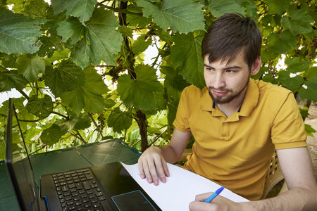 a young businessman is working at a computer in the garden on a sunny summer day the concept of remote work at home. high quality photoの写真素材