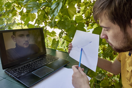 a young businessman is working at a computer in the garden on a sunny summer day the concept of remote work at home. high quality photoの写真素材