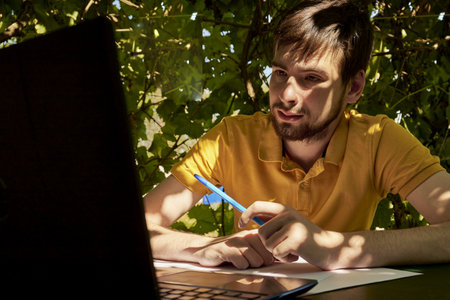 a young businessman is working at a computer in the garden on a sunny summer day the concept of remote work at home. high quality photoの写真素材