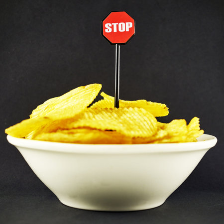 potato chips in a plate and a stop sign on a black background the concept of limiting consumption health. high quality photoの写真素材