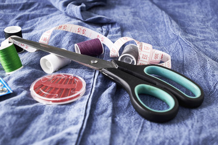 scissors needles measuring tape and thread on the background of torn jeans the concept of reasonable consumption of needlework for small businesses. high quality photoの写真素材