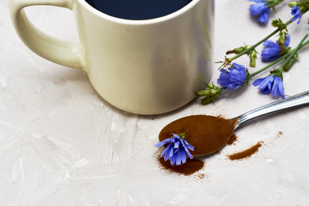 a mug with a drink of chicory chicory flowers and a spoon with powder and a chicory flower on the table. high quality photoの写真素材