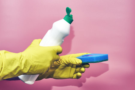 a man in rubber household gloves pours detergent from a bottle onto a sponge on a pink background. high quality photoの写真素材