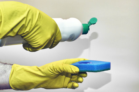 a man in rubber household gloves pours detergent from a bottle onto a sponge on a light background. high quality photoの写真素材