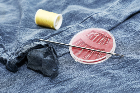 needles and thread on the background of torn jeans the concept of reasonable consumption of needlework for small businesses. high quality photoの写真素材