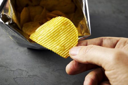 A hand takes potato chips from a packの写真素材