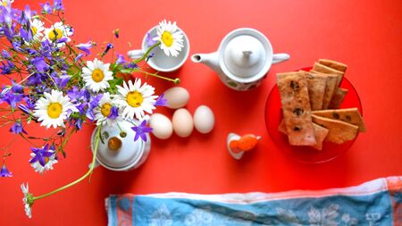 flowers, eggs, cookies and tea set on a red table, breakfastの写真素材
