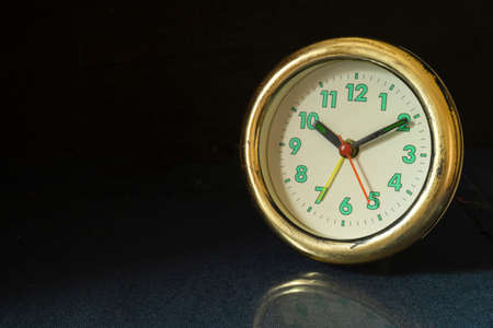 The Old round watch on black background. The Alarm clock on table with reflection. Green numbers and black arrows beside mechanical hoursの写真素材